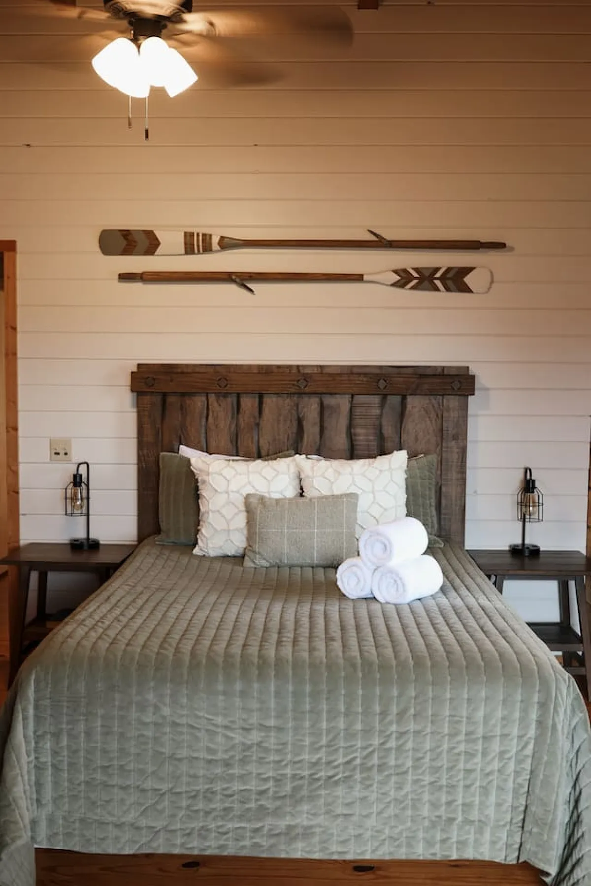 This image showcases a bedroom with a wooden bed frame, decorative paddles on the wall, and textured bedding. The setting feels cozy and serene, with soft lighting and rustic accents that evoke the tranquil atmosphere of a mountain retreat.