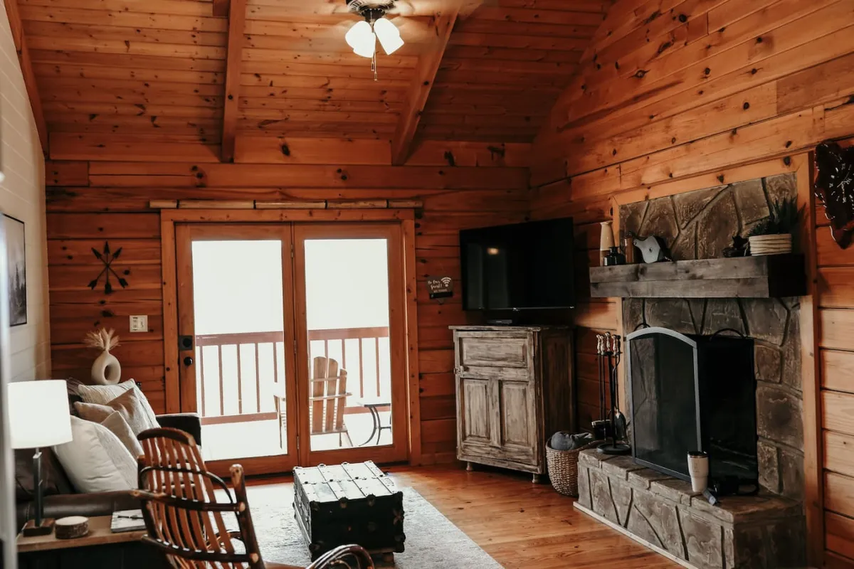 This photo features an inviting interior with a glowing fireplace, French doors leading to more scenic views, and wooden furnishings that create a warm, rustic ambiance. A TV offers modern entertainment options, and the spacious seating area encourages relaxation and togetherness.