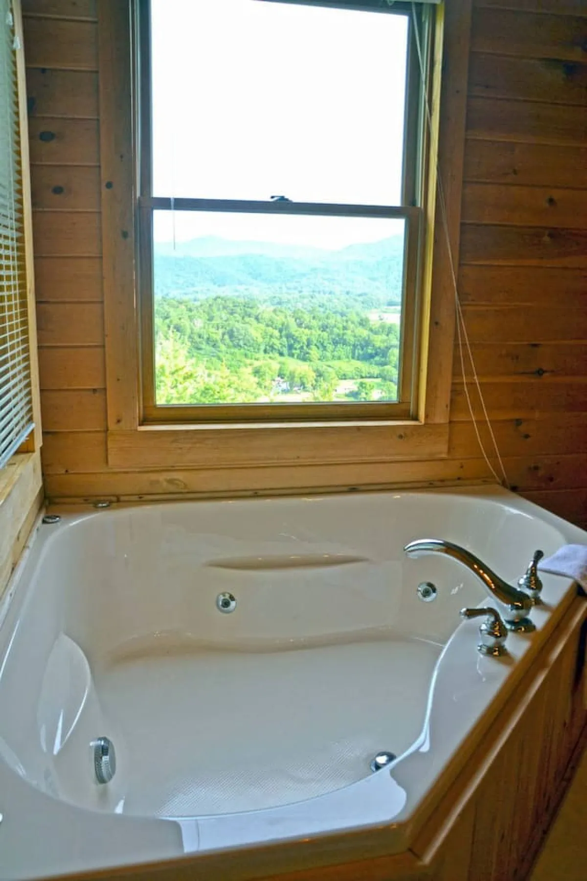 A luxurious indoor jacuzzi tub is set beside a large window, which frames a panoramic view of the mountains outside. Natural light floods the space, blending the comforts of the interior with the stunning beauty beyond. The scene suggests a tranquil and indulgent soak after a day of adventure.
