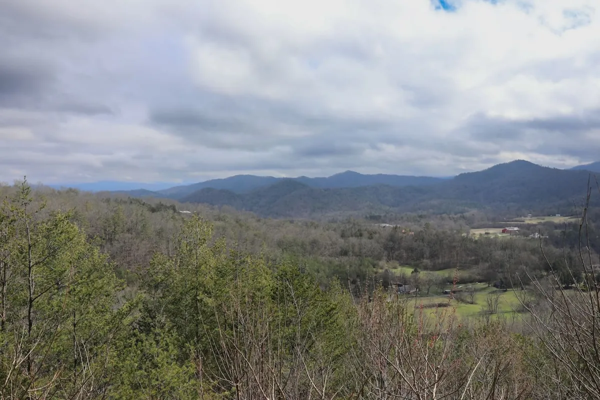 A breathtaking panoramic view capturing a mountain range enveloped by dense forests and a sprawling valley. The sunset casts a warm glow over the landscape, inviting thoughts of hiking, nature observation, and peaceful reflection. The scene hints at abundant wildlife and the tranquil mood of the Smoky Mountains, with layers of greenery stretching toward the horizon.